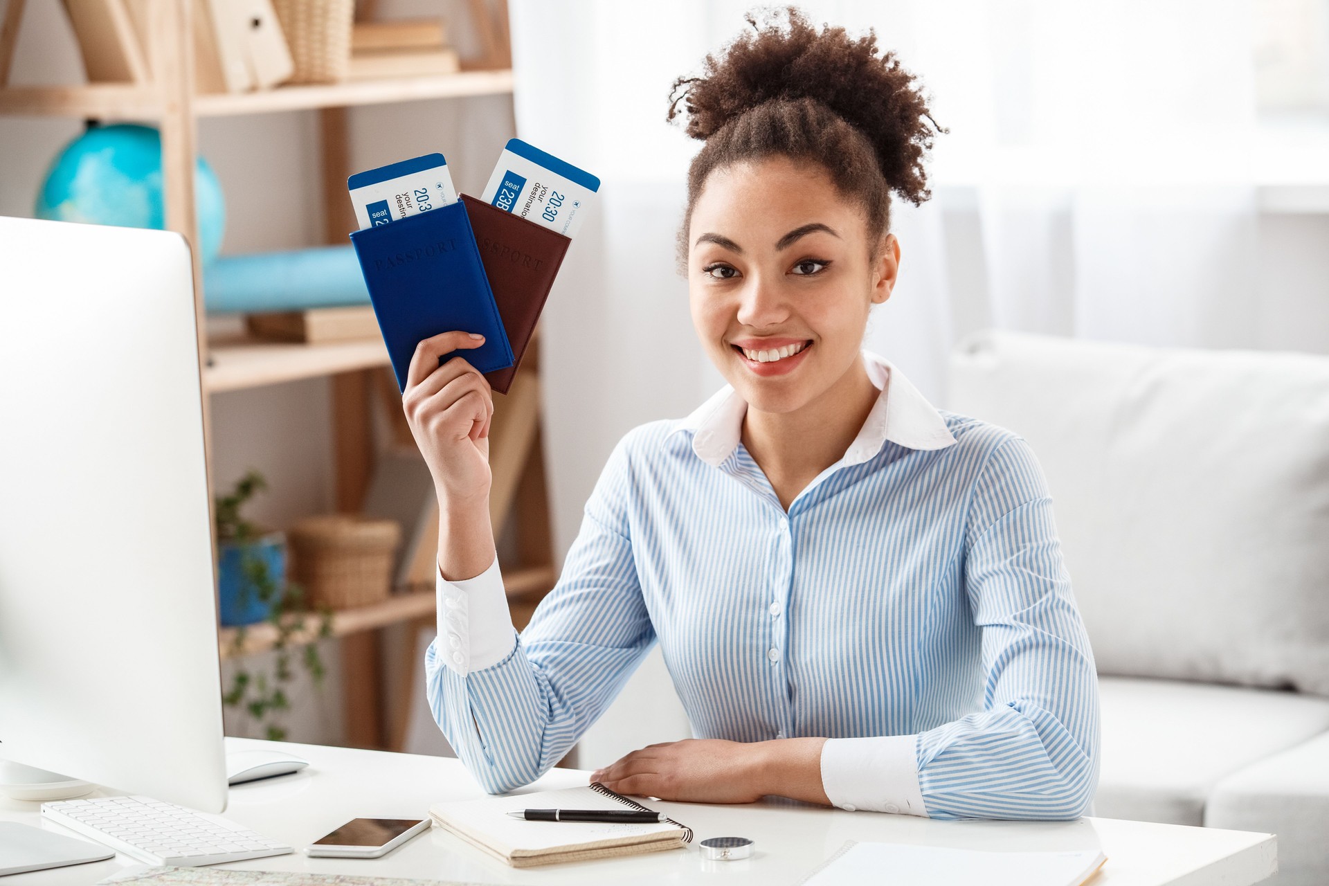 Tour agent sitting at table in office holding passports and tickets looking camera cheerful